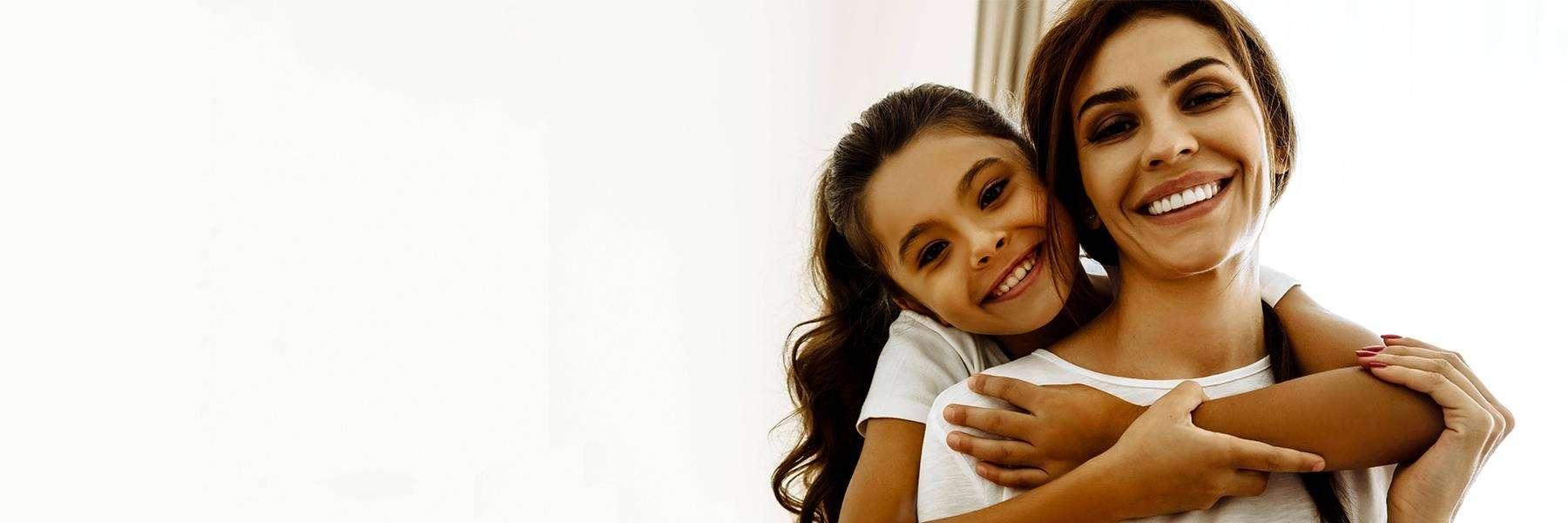 woman smiling while daughter hugs her from behind