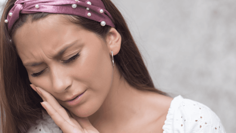 A young woman with a headband and white top touching her cheek, appearing to be in pain.