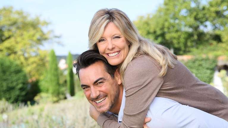 Man carrying his wife as they smiles with their clean teeth in Northborough MA