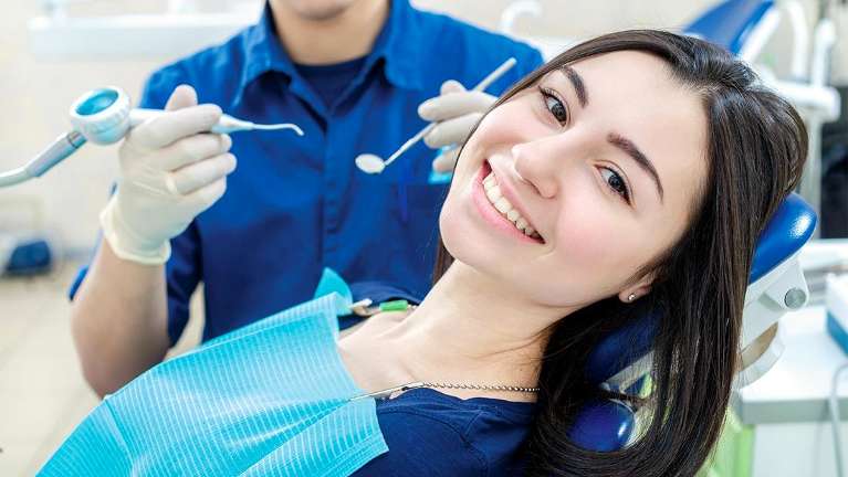 An image of a woman sitting on a dental chair, with a bright smile on her face