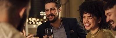 man holding wine glass sitting next to smiling woman at dinner party